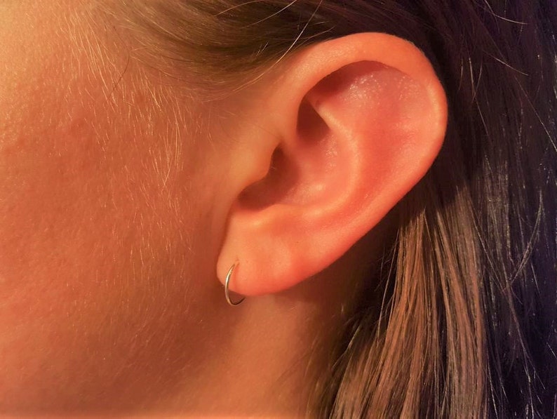 May include: A close-up of a person's ear with a small silver hoop earring in the lobe.