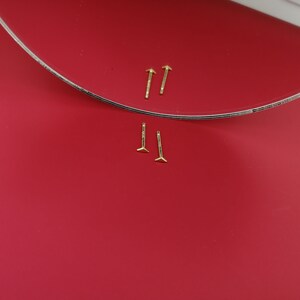 May include: Two pairs of gold stud earrings on a red background. The earrings are small and have a simple design.