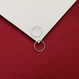 May include: Two silver hoop earrings on a red and white background.