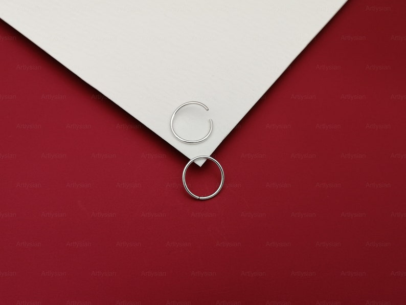 May include: Two silver hoop earrings on a red and white background.