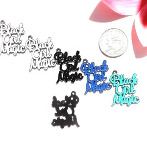 May include: Six metal charms featuring the text Black Girl Magic in various colors including silver, black, blue, and turquoise. A US quarter coin is included for scale, measuring approximately 0.955 inches in diameter.
