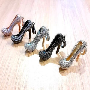 May include: Five sparkly high heel shoe charms in different colors, including silver, black, and white. The charms are made of metal and have a rhinestone design.