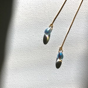 May include: A pair of delicate gold chain earrings with iridescent teardrop-shaped glass charms.