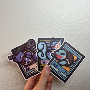 May include: Three cartoon character trading cards featuring blue and green characters with a white background. The cards have black borders and text that reads "66" and "20".