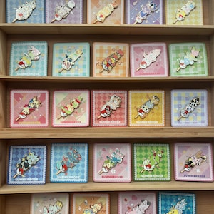 May include: A collection of twenty enamel pins arranged on square backing cards, each featuring a stack of three stylized creatures on a stick. The cards display various pastel checkered patterns and the text SUMMERROSE at the bottom.