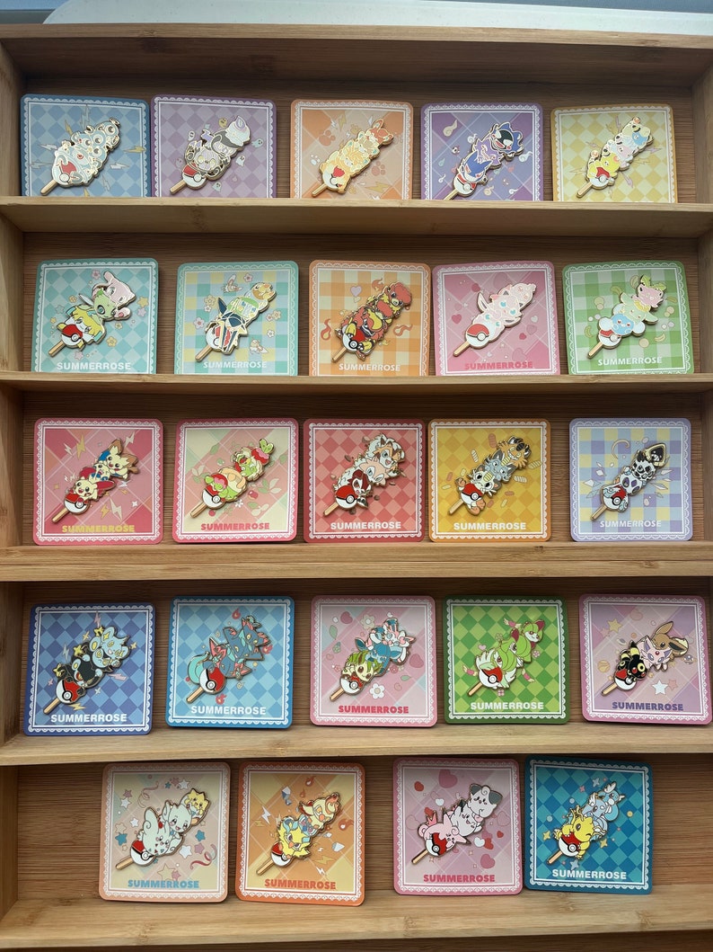 May include: A collection of twenty enamel pins arranged on square backing cards, each featuring a stack of three stylized creatures on a stick. The cards display various pastel checkered patterns and the text SUMMERROSE at the bottom.