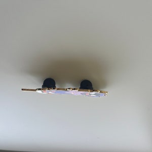 May include: A metal enamel pin viewed from the side, showing the thin profile of the decorative piece. Two black rubber clutch backings are attached to the metal posts on the reverse side of the pin, which features gold-toned metal edges.