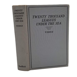 May include: A vintage book with a light blue cover titled "Twenty Thousand Leagues Under The Sea" by Jules Verne. The book is published by Saalfield.