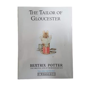 Può includere: La copertina del libro Il sarto di Gloucester con un topo seduto su un rocchetto di filo, che legge un giornale. Il libro è di Beatrix Potter ed è l'edizione originale e autorizzata con nuove riproduzioni a colori. La copertina è blu chiaro con testo bianco.