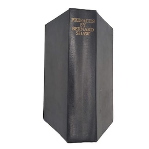 Pode incluir: Um livro preto de capa dura com letras douradas na lombada que diz "PREFACE BY BERNARD SHAW".