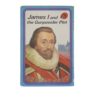 Op de afbeelding: Een blauwe en witte boekomslag met de titel "James I en de poedercomplot". De omslag toont een portret van koning Jacobus I in een rode en gouden mantel met een witte kraag. Een rode lieveheersbeestje bevindt zich in de rechterbovenhoek.