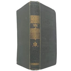 Pode incluir: Um livro de capa dura verde-escuro com uma lombada gravada a ouro apresentando o texto "DICKENS NOVELS", "SKETCHES BY BOZ" e "ROUTLEDGE". A lombada inclui padrões florais e geométricos, enquanto a capa exibe um design em relevo sutil.