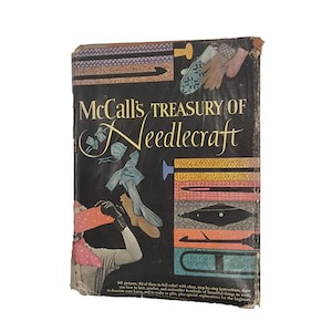 May include: A vintage book titled "McCall's Treasury of Needlecraft" with a black cover. The cover features illustrations of needlecraft items and text. The book's cover is slightly worn, suggesting its age.