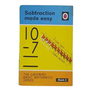 May include: A yellow and blue book cover with the title "Subtraction made easy" and a red ladybug logo. The book cover features a math problem with the equation "10 - 7" and a visual representation of the problem using red flowers.