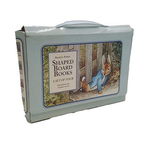 Peut inclure: Un coffret bleu clair contenant quatre livres cartonnés façonnés de Beatrix Potter. La boîte présente une illustration de Pierre Lapin. Le texte sur la boîte indique "SHAPED BOARD BOOKS A SET OF FOUR Retold from the original stories."