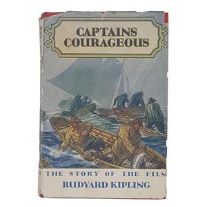 May include: Vintage hardcover book titled "Captains Courageous" with a nautical illustration. The cover features a painting of several small boats on a choppy sea, with the title in a decorative banner. The author's name, Rudyard Kipling, is also visible.