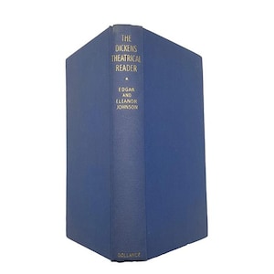 Pode incluir: Um livro de capa dura azul intitulado The Dickens Theatrical Reader de Edgar e Eleanor Johnson. A lombada apresenta letras douradas com o título, os nomes dos autores e o nome da editora Gollancz na parte inferior, sobre uma capa azul sólida.
