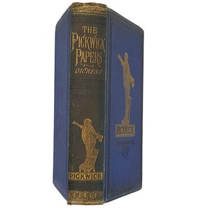 Pode incluir: Um livro de capa dura azul com letras douradas na lombada. O título é "The Pickwick Papers" de Dickens. O livro tem uma ilustração dourada de um homem na capa.