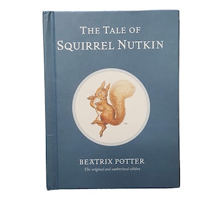 May include: A blue book cover with the title "The Tale of Squirrel Nutkin" and an illustration of a squirrel. The author, Beatrix Potter, is listed below the title with the text "The original and authorized edition."