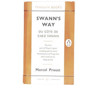 Op de afbeelding: Vintage Penguin Books editie van "Swann's Way" van Marcel Proust. Het boek heeft een witte en oranje omslag met de titel in zwarte letters. De omslag bevat ook het Penguin-logo en de tekst "Du Côté de Chez Swann".