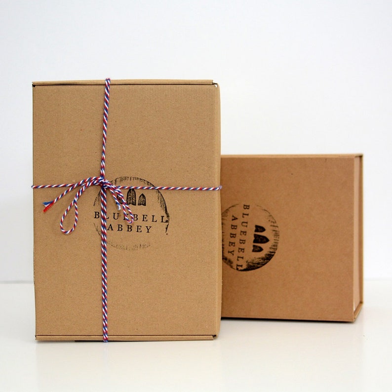 Op de afbeelding: Twee bruine kartonnen dozen met een rood-wit-blauw touw eromheen gebonden. De dozen zijn gelabeld met "Bluebell Abbey" en een afbeelding van een gebouw.