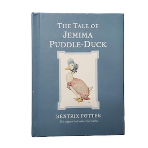 Puede incluir: Una cubierta de libro azul con el título "The Tale of Jemima Puddle-Duck" en texto blanco. La cubierta presenta una ilustración de un pato con un vestido rosa y un gorro azul. El autor, Beatrix Potter, está impreso debajo de la ilustración.