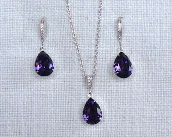 May include: A silver necklace and earrings set with a teardrop-shaped purple gemstone pendant.
