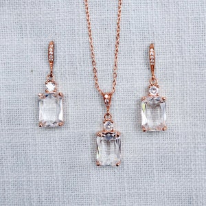 May include: A rose gold necklace and earrings set with a rectangular clear crystal pendant and matching earrings.