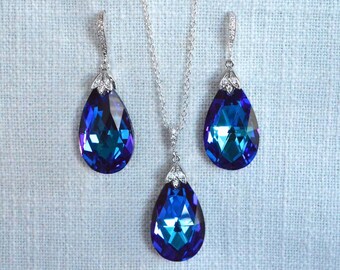 May include: A silver necklace and earrings set with teardrop-shaped blue crystal pendants. The crystals have a deep blue color with a hint of purple.