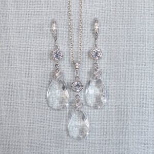 May include: A silver necklace and earrings set with teardrop-shaped crystal pendants and clear round stones.