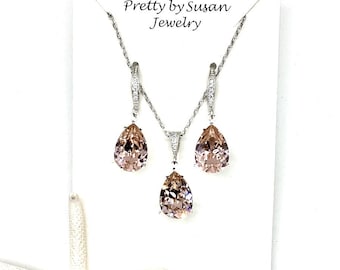 May include: A jewellery set featuring a necklace and matching earrings with pear-shaped peach-coloured crystals set in silver-toned metal. The display card reads Pretty by Susan Jewelry. A white starfish is positioned at the bottom left corner.