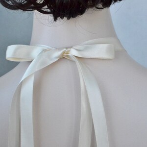 May include: A white satin ribbon tied in a bow at the back of the neck. The ribbon is long enough to tie in a bow at the back of the neck.