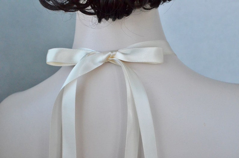 May include: A white satin ribbon tied in a bow at the back of the neck. The ribbon is long enough to tie in a bow at the back of the neck.