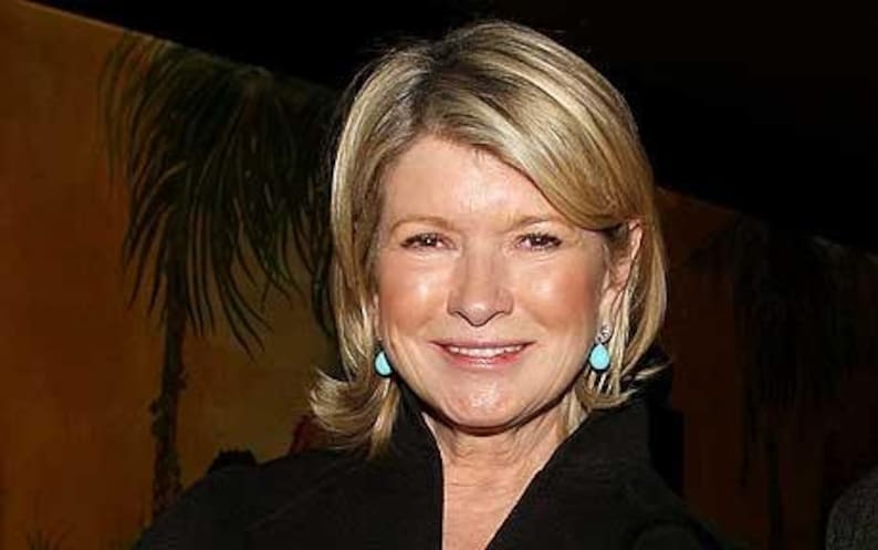 May include: A woman with blonde hair wearing a black blazer and turquoise earrings. She is smiling and looking at the camera.