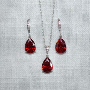 Peut inclure: Un collier et des boucles d'oreilles en argent avec des pierres précieuses rouges en forme de goutte et des accents clairs.