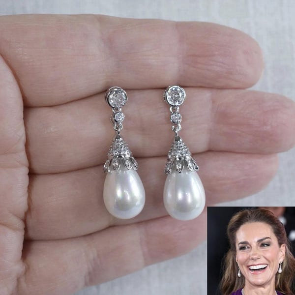 May include: A pair of silver-toned drop earrings featuring a teardrop-shaped white pearl suspended from a decorative cap encrusted with small clear stones, topped with two additional round clear stones in a vertical setting on each earring.