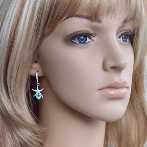 Puede incluir: Un maniqu&iacute; con cabello rubio que lleva un par de aretes colgantes de plata con una piedra preciosa azul y un dije de estrella de mar.