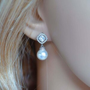 May include: Silver dangle earrings with a clear square crystal and a white pearl drop.