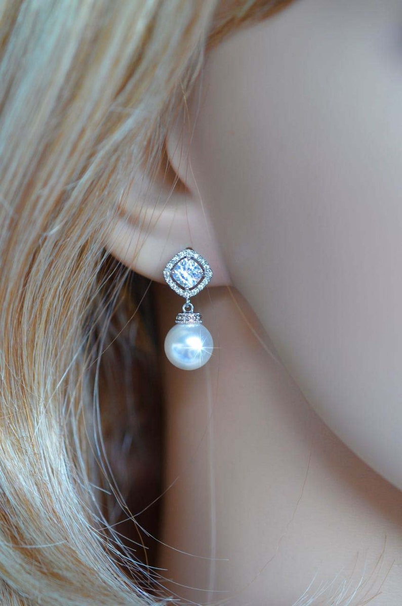 May include: Silver dangle earrings with a clear square crystal and a white pearl drop.