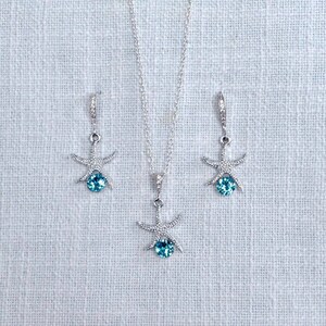 Puede incluir: Un conjunto de collar y pendientes de plata con un colgante de estrella de mar con una piedra preciosa azul.