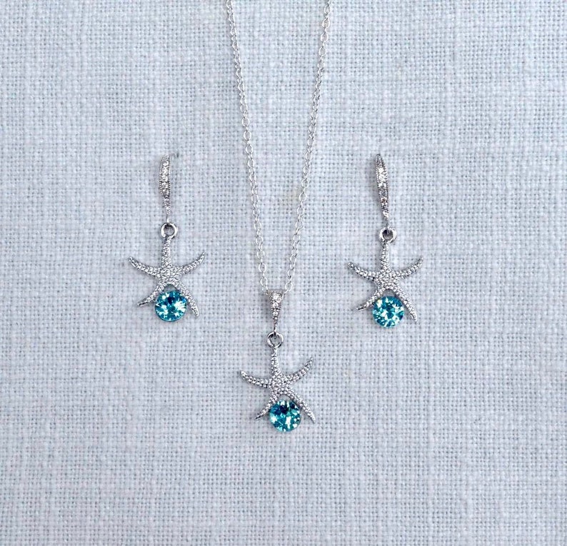 Puede incluir: Un conjunto de collar y pendientes de plata con un colgante de estrella de mar con una piedra preciosa azul.