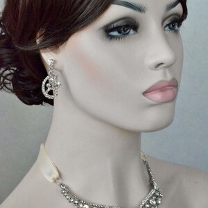 May include: A silver necklace with a delicate, ornate design featuring a cascade of sparkling rhinestones. The necklace is paired with matching earrings, also adorned with rhinestones.