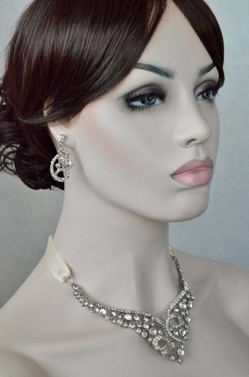 May include: A silver necklace with a delicate, ornate design featuring a cascade of sparkling rhinestones. The necklace is paired with matching earrings, also adorned with rhinestones.