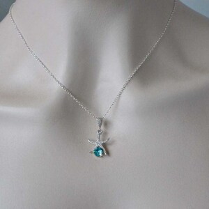 Puede incluir: Un collar de cadena de plata con un colgante de estrella de mar con una piedra preciosa azul.