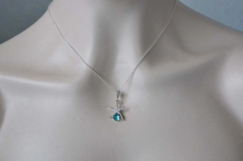 Puede incluir: Un collar de cadena de plata con un colgante de estrella de mar con una piedra preciosa azul.