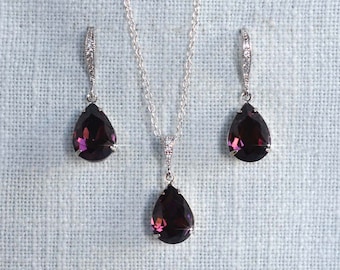 May include: A silver necklace and earrings set with teardrop-shaped purple crystals.