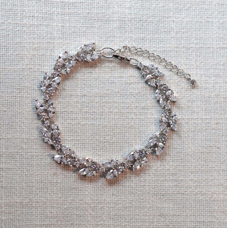 May include: A silver bracelet with a delicate design of leaves and sparkling stones.