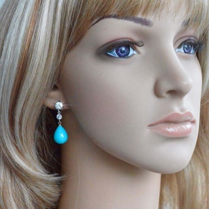May include: A pair of dangle earrings with a turquoise teardrop stone and clear cubic zirconia accents.