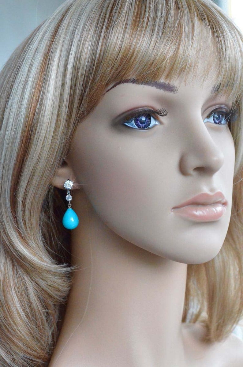 May include: A pair of dangle earrings with a turquoise teardrop stone and clear cubic zirconia accents.