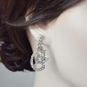 May include: Silver dangle earrings with a cluster of clear rhinestones in a teardrop shape.